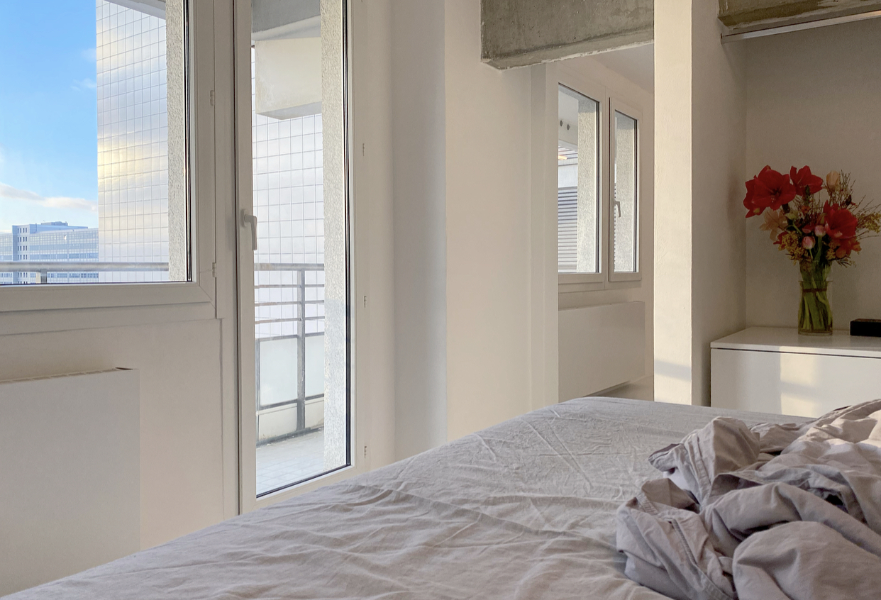 Open Forum Living 44 — bedroom with balcony door open, exposed concrete beam, city view