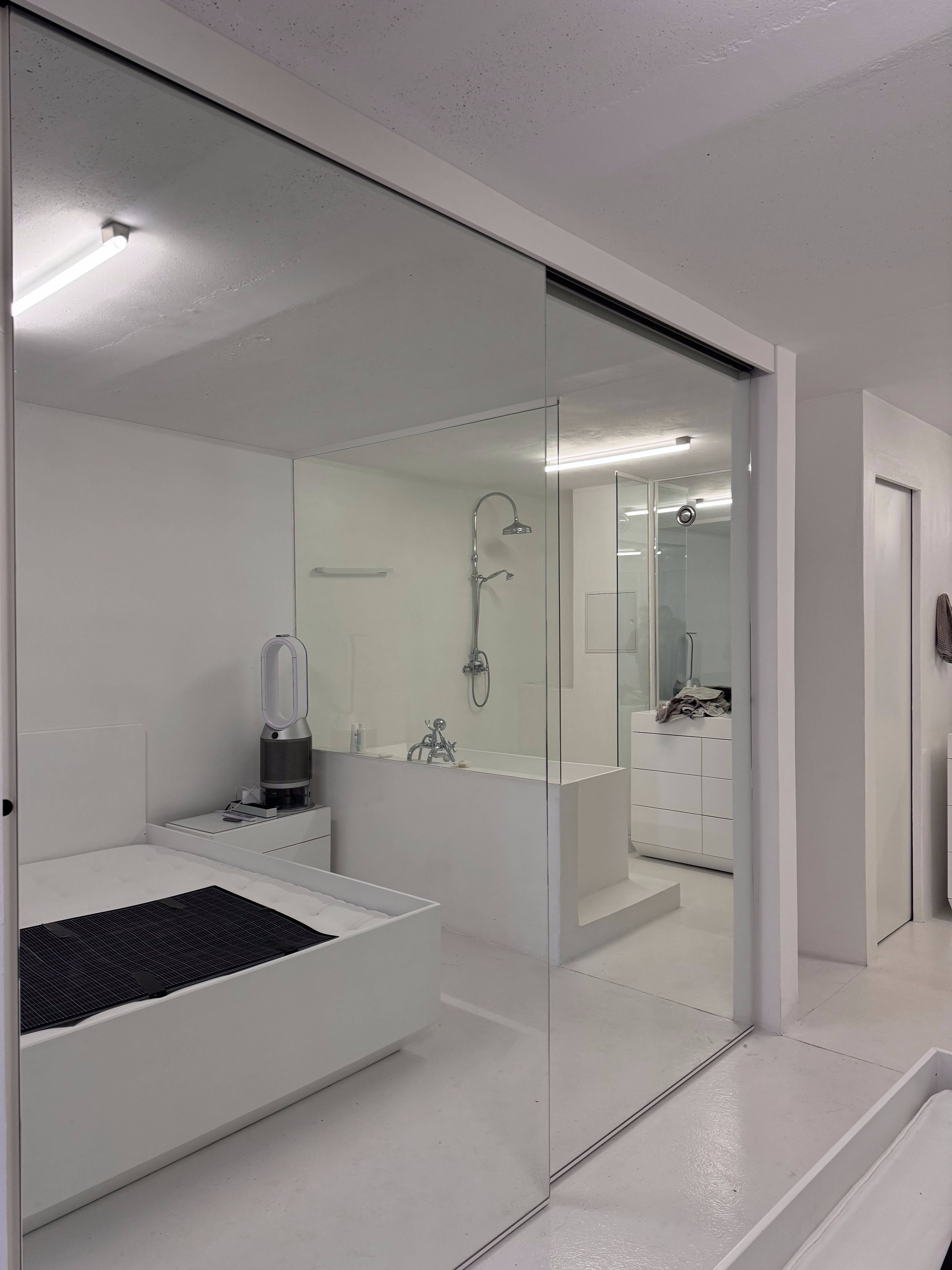 Open Forum Living 44 — glass-walled wet room, all white, open to bedroom